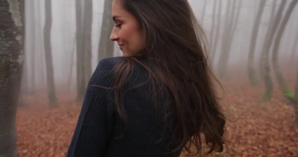 Autumn vibes, foggy forest. Attractive brunette woman with long hair wears casual outfit and walks across the forest covered with fallen leaves. Positive emotions, happiness, whirling — Stock Video