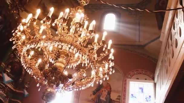 Orthodoxe, Christendom, kerk. Lichtstraal schijnt over oude gondel kroonluchter met kaarsen opknoping van de top van een hoog plafond met kunst — Stockvideo