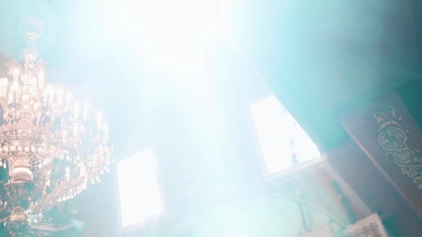 Ορθόδοξη, Χριστιανισμός, εκκλησία. Ακτίνα του φωτός λάμπει πέρα από το παλαιό gondel πολυέλαιο με κεριά που κρέμονται από την κορυφή του ψηλή οροφή με έργα τέχνης — Αρχείο Βίντεο