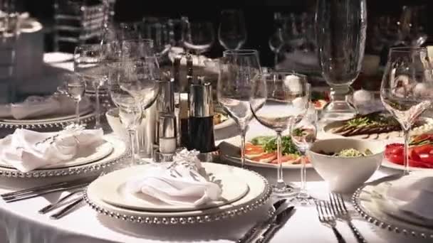 Recepción, celebrando en el restaurante. Grandes mesas redondas blancas decoradas con flores blancas y deliciosos puestos de comida en la sala llena de luz — Vídeos de Stock