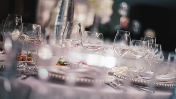 Recepção, comemorando no restaurante. Grandes mesas brancas redondas decoradas com flores brancas e deliciosos stands de comida no salão tha cheio de luz — Vídeo de Stock