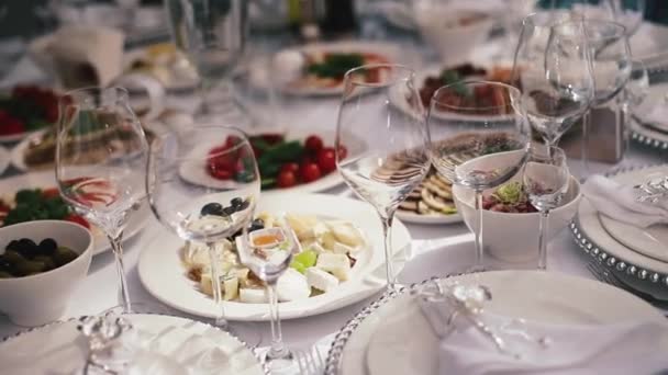 Recepción, celebrando en el restaurante. Grandes mesas redondas blancas decoradas con flores blancas y deliciosos puestos de comida en la sala llena de luz — Vídeos de Stock