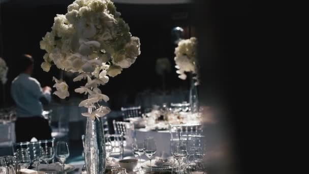 Recepción, celebrando en el restaurante. Grandes mesas redondas blancas decoradas con flores blancas y deliciosos puestos de comida en la sala llena de luz — Vídeos de Stock