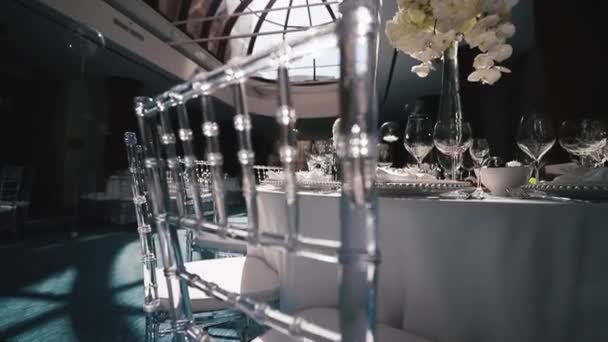 Recepción, celebrando en el restaurante. Grandes mesas redondas blancas decoradas con flores blancas y deliciosos puestos de comida en la sala llena de luz — Vídeo de stock