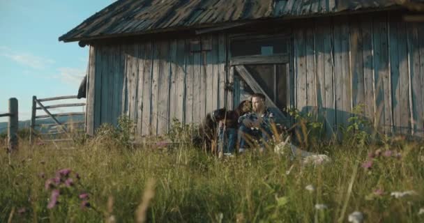 Berg land lovestory. 4 k. Man en vrouw geniet van 's avonds lichten zitten op de veranda met hun twee honden - / bermann en Labrador Retriever — Stockvideo