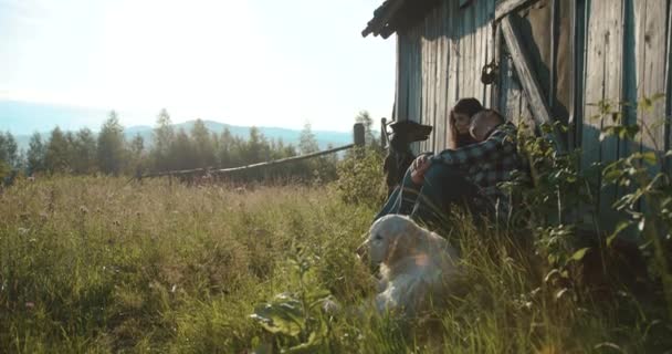 Berg land lovestory. 4 k. Man en vrouw geniet van 's avonds lichten zitten op de veranda met hun twee honden - / bermann en Labrador Retriever — Stockvideo