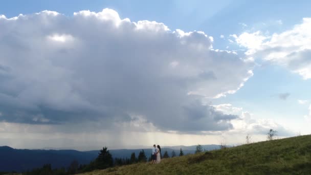 Luftaufnahme. 4k. Mann und Frau halten sich auf dem Hügel unter dicken Wolken über den Bergen an den Händen — Stockvideo