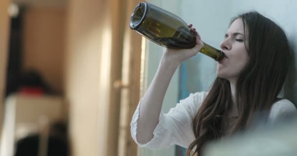 Žena v depresi. Mladá brunetka sedí na podlaze a pije víno z láhve brečící. 4k — Stock video