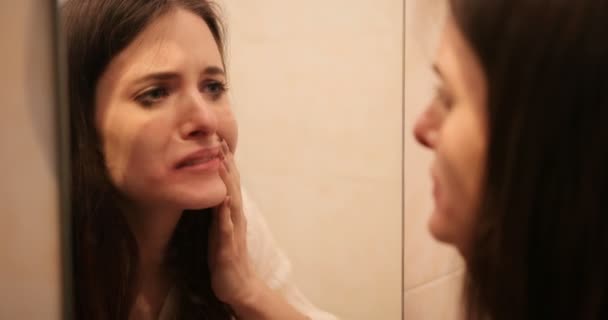 Triste donna depressa con lunghi capelli bruni piange in piedi davanti a uno specchio in bagno. 4k — Video Stock