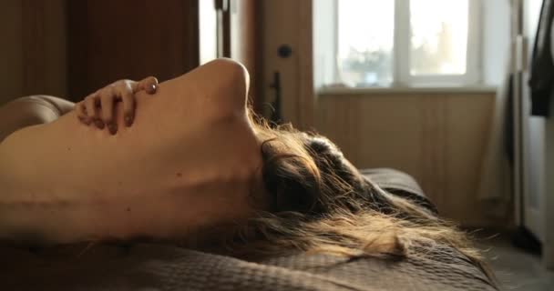 Молода пригнічена жінка з довгим темним волоссям лежить на ліжку перед дзеркалом і подряпається. Концепція хвороби. 4k — стокове відео