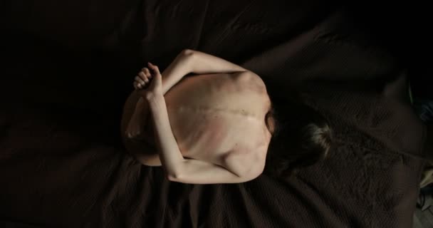 Concepto de víctima. Joven morena flaca con cabello oscuro sostiene sus manos detrás de su espalda arañada sentada en la cama — Vídeos de Stock