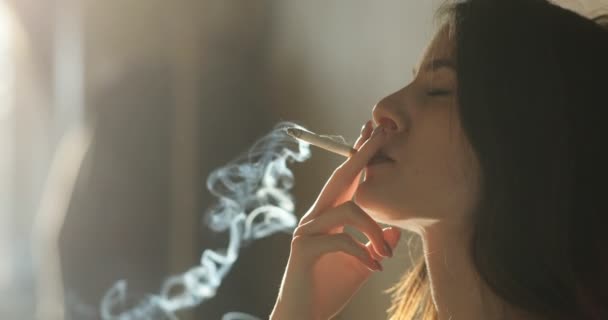 Depressed woman. Young girl with long brunette hair smokes a cigar sitting on the floor indoor in the evening lights. 4k — Stock Video