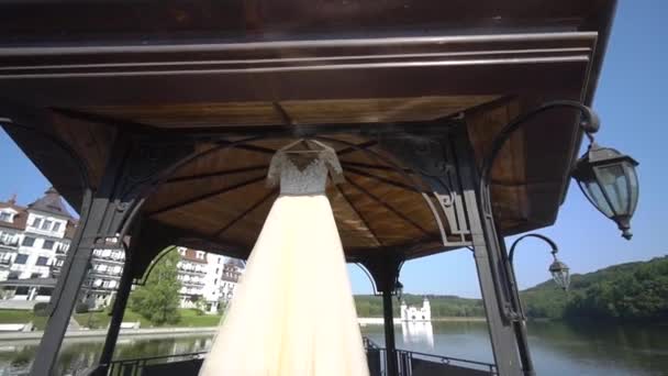 ウェディングドレスは、湖の近くのアーバーの重さです。晴れた日. — ストック動画