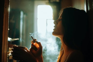 Zarif sutyen ve estetik duvara geri oturan genç güzel kadın sigara içiyor