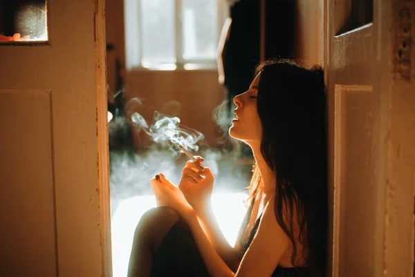 Jeune femme béatifique assis dos au mur en soutien-gorge élégant et esthétique fume cigarette — Photo