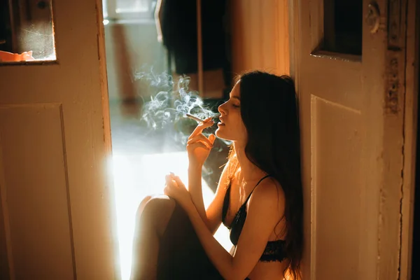 Jeune femme béatifique assis dos au mur en soutien-gorge élégant et esthétique fume cigarette — Photo