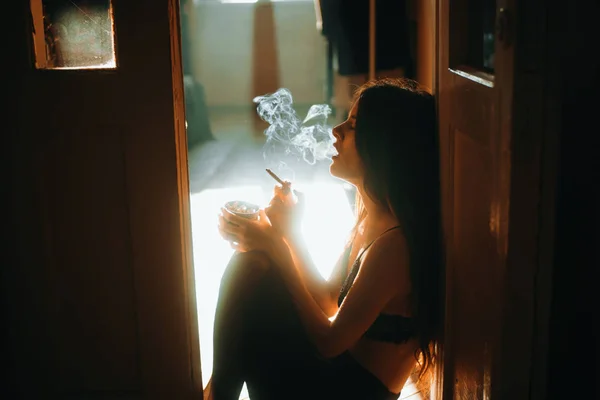 Joven mujer beata sentada de nuevo a la pared en un elegante sujetador y cigarrillos estéticos —  Fotos de Stock