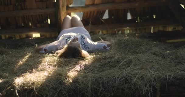 Jeune femme souriant aux rayons du soleil sur le foin. Un hangar en bois. 4K . — Video