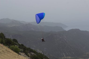 Dağların üzerinden uçan bir adam bir paraşüt içinde. Parasailin