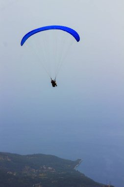 Dağların üzerinden uçan bir adam bir paraşüt içinde. Parasailin