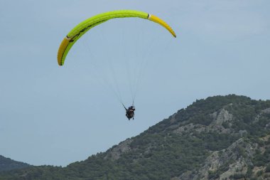 Dağların üzerinden uçan bir adam bir paraşüt içinde. Parasailin