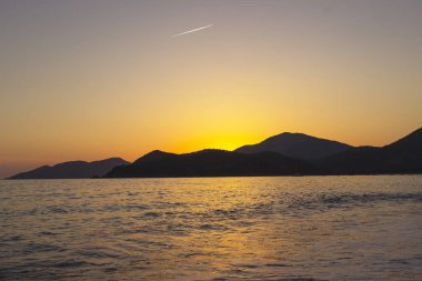 Akdeniz manzara. Günbatımı parlak akan ile denizde bulutların arasından güneş ışınlarının renkli. Dağları'nın siluetleri. Adam