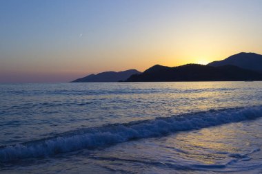 Akdeniz manzara. Günbatımı parlak akan ile denizde bulutların arasından güneş ışınlarının renkli. Dağları'nın siluetleri. Adam