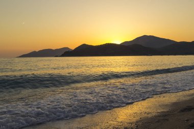 Akdeniz manzara. Günbatımı parlak akan ile denizde bulutların arasından güneş ışınlarının renkli. Dağları'nın siluetleri. Adam