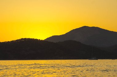Akdeniz manzara. Günbatımı parlak akan ile denizde bulutların arasından güneş ışınlarının renkli. Dağları'nın siluetleri. Adam