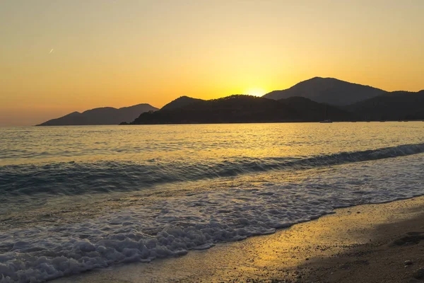 Akdeniz manzara. Günbatımı parlak akan ile denizde bulutların arasından güneş ışınlarının renkli. Dağları'nın siluetleri. Adam