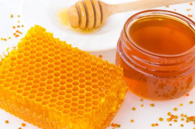 Petek ve kavanoz karanlık bal. Bir uçan daire üzerinde kepçe tatlım. Polen beyaz bir arka plan üzerinde dağınık olduğunu