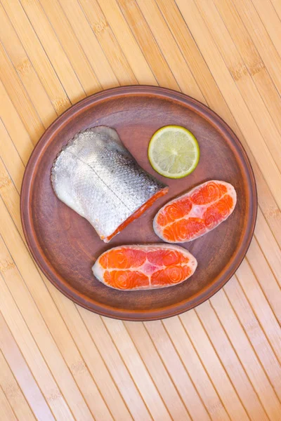 Sliced salmon and a slice of lemon on a ceramic plate. Wooden bamboo background. Top view