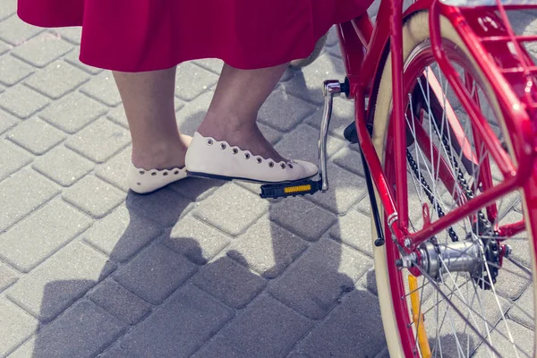 Koncept: kvinnor på en cykel. Flickan i den röda kjolen sätter sin fot på cykel pedalen. Del av bilden — Stockfoto