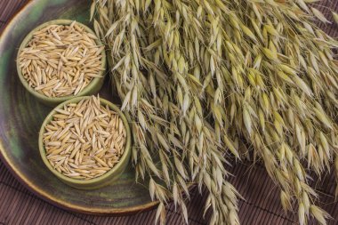 İki kase yulaf tahıl ve yulaf hasat yeşil bir plaka üzerinde.