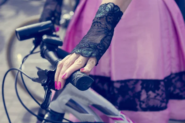 Concept: women on bicycles. Hands holding the handlebars. Pink skirt with black lace