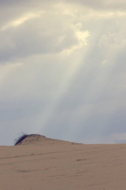 Bulutların arasından geçen güneş ışınları kum ulanında parlıyor.