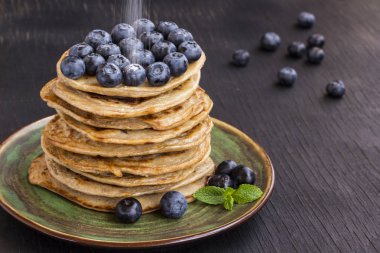 Siyah masada yeşil bir tabakta yaban mersini ve pudra şekeri ile lezzetli gözleme
