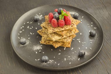 Tüm tahıl ile kurabiye. Üstünde ahududu ve yaban mersini meyveleri. Siyah plaka, siyah arka plan