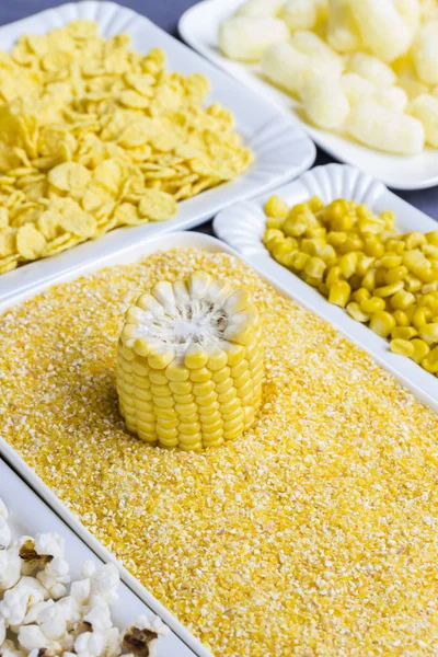 Raw corncob, cornmeal, corn sticks and flakes in white plates, top view