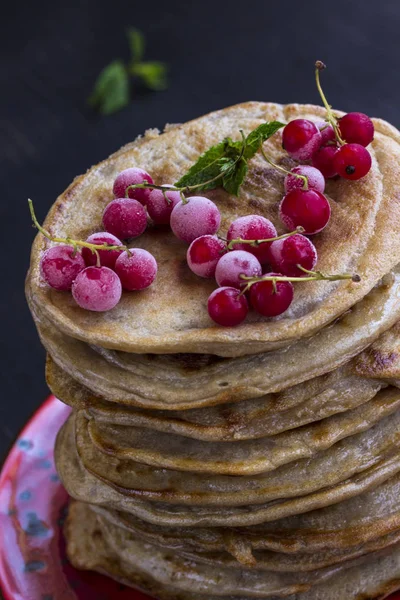Delicious pancake with frozen red currants on black table