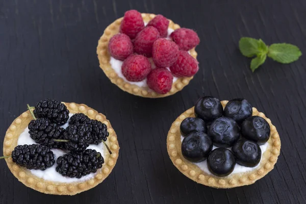 Basket-shaped cookies with raspberry, blueberry and blackberry berries. Black background