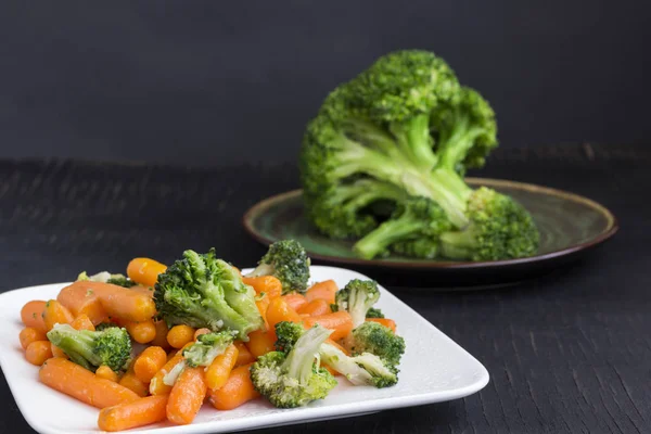 Vihannessalaatti: parsakaali ja porkkanat valkoisella lautasella mustalla pohjalla — kuvapankkivalokuva