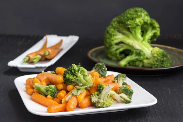 Vegetable salad: broccoli and carrots in a white plate on a black background — Stock Photo, Image