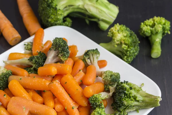 Grönsakssallad: broccoli och morötter i vit plåt på svart bakgrund — Stockfoto