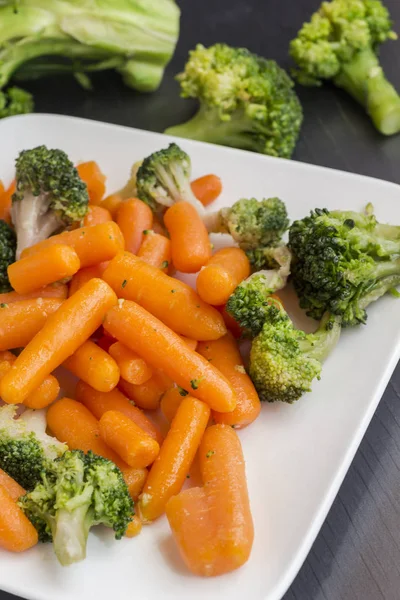 Grönsakssallad: broccoli och morötter i vit plåt på svart bakgrund — Stockfoto