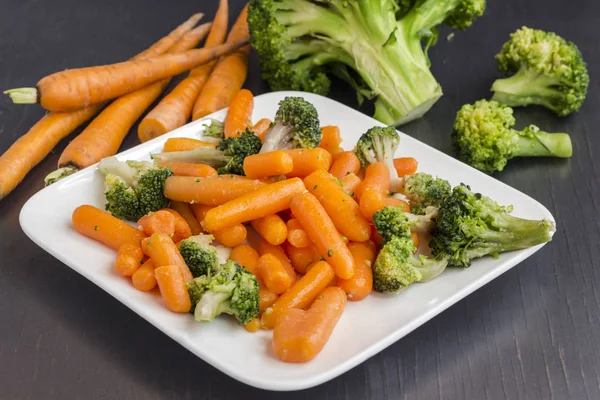 Sebze salatası: brokoli ve havuç siyah bir arka plan üzerinde beyaz bir tabakta — Stok fotoğraf