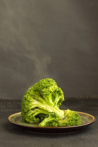 Kokt kål broccoli i en tallrik på en svart bakgrund. Ånga på kål — Stockfoto