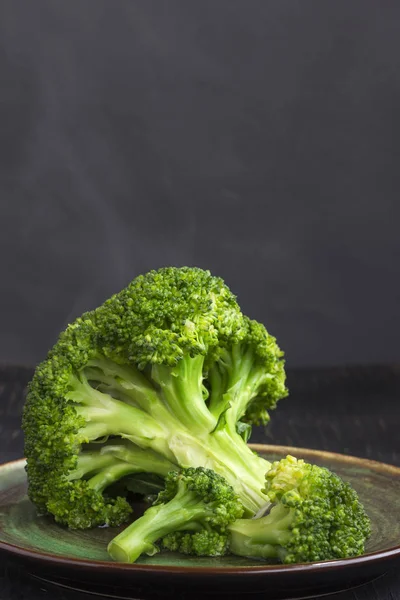 Broccoli de varză fiartă într-o farfurie pe un fundal negru. Aburul pe varză — Fotografie, imagine de stoc