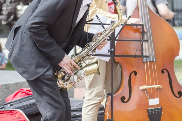 Street musician\'s hands playing saxophone and double-bass in an urban environment