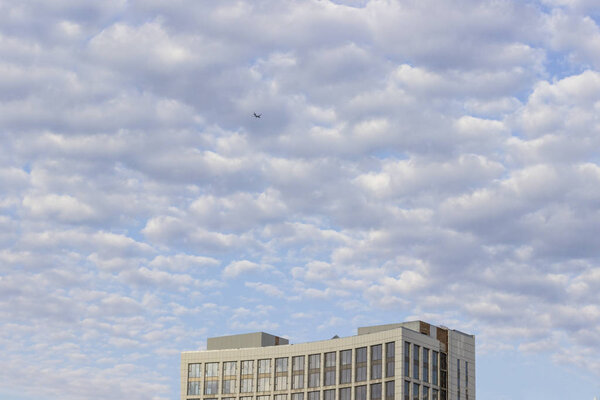 Airplane on a blue sky with white cumulus clouds. Part of the building at the bottom of the frame